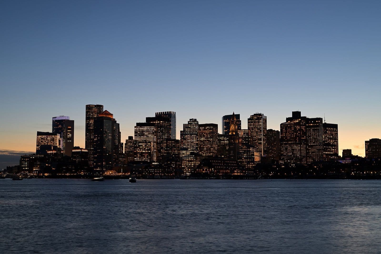 Boston's Financial District skyline at dusk across the harbor